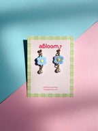Flower-shaped earrings on a 'abloom' branded card against a colorful background