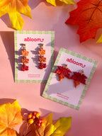 Two pairs of dangling leaf-shaped earrings displayed on branded cards.