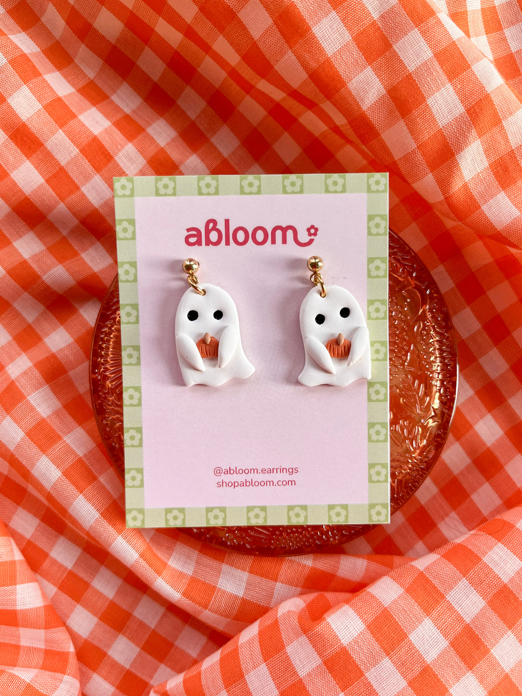 Cute handmade ghost earrings holding tiny pumpkins with whimsical Halloween design