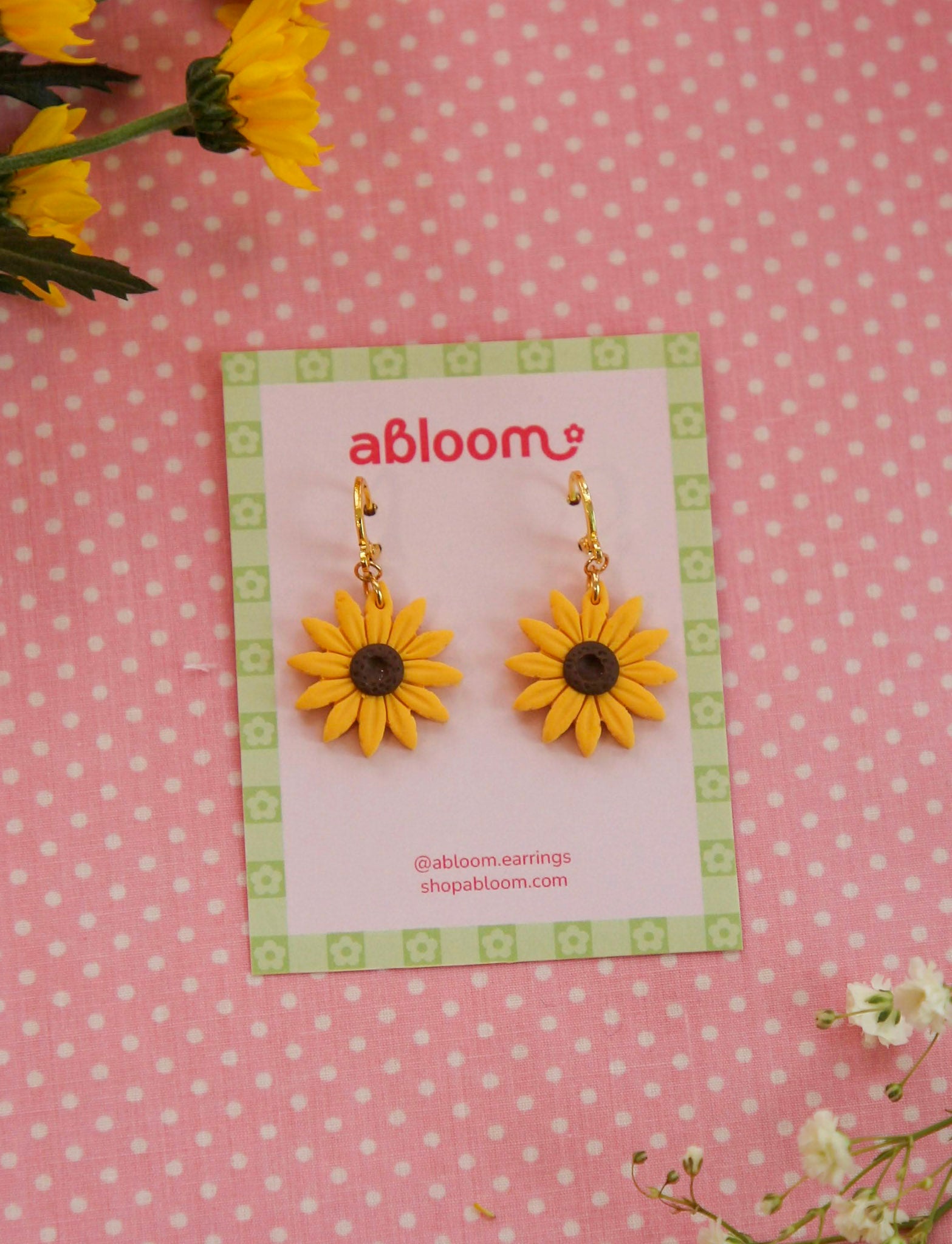 Bright Yellow sunflower earrings on a 'abloom' branded card against a pink polka dot background.