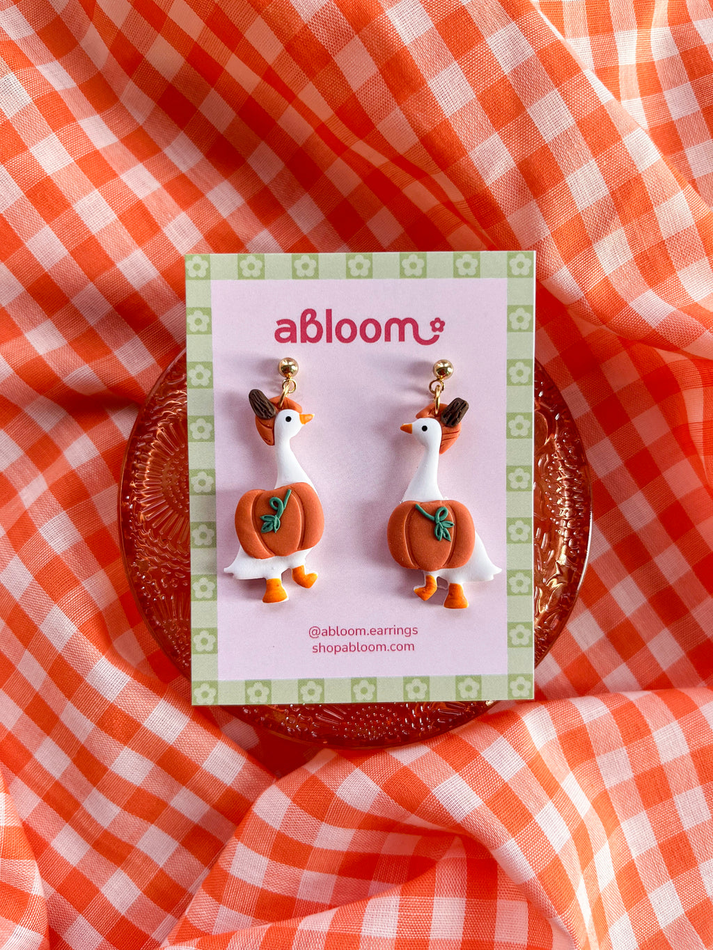 A pair of whimsical polymer clay earrings of white geese in a orange pumpkin costume