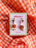 A pair of whimsical polymer clay earrings of white geese in a orange pumpkin costume