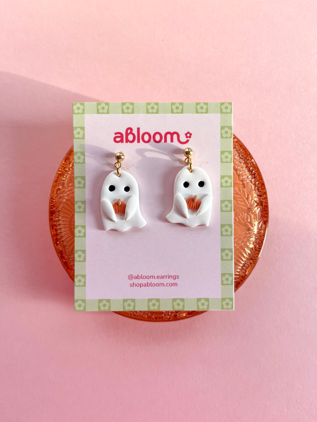 Cute handmade ghost earrings holding tiny pumpkins with whimsical Halloween design