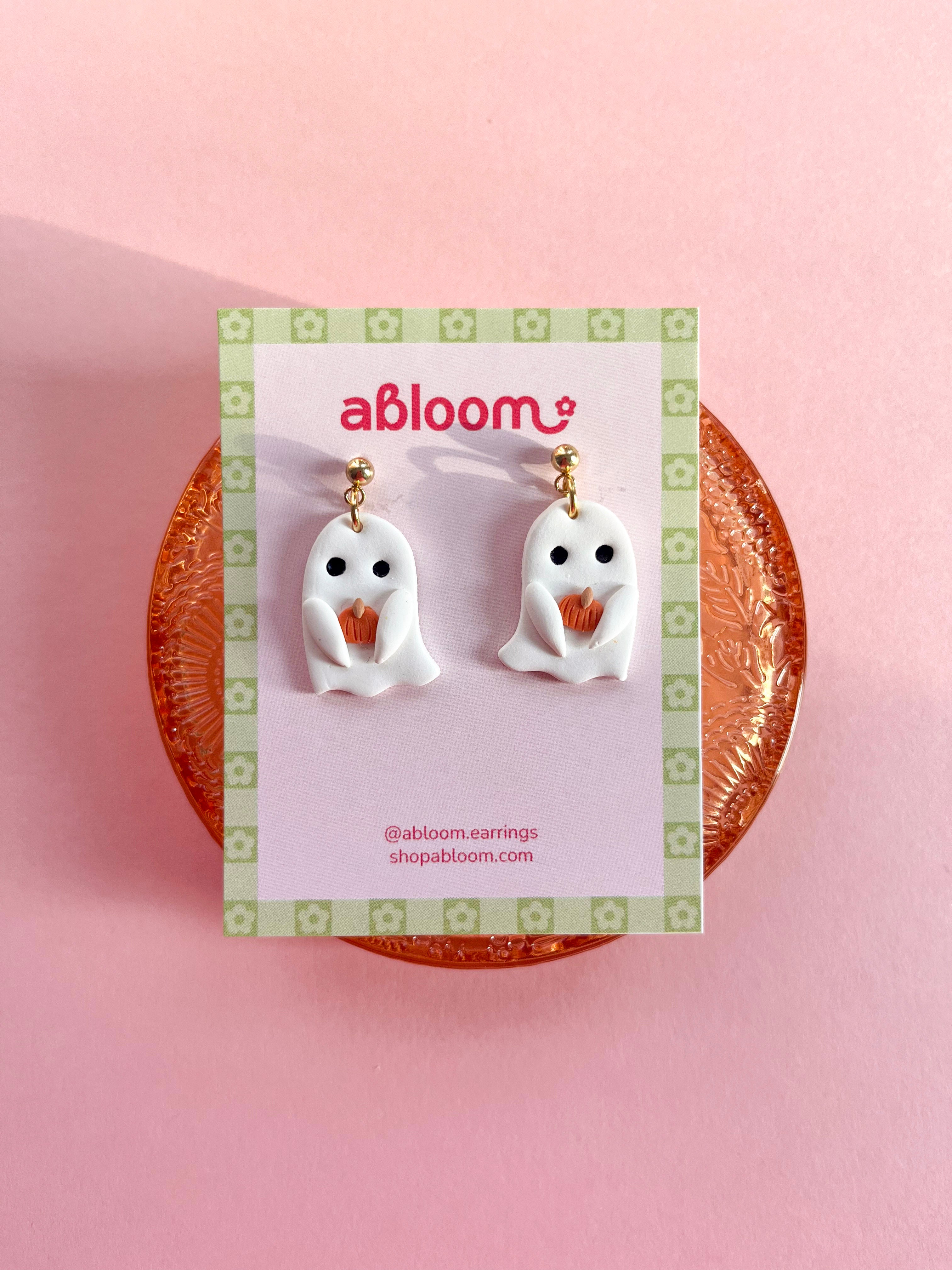Cute handmade ghost earrings holding tiny pumpkins with whimsical Halloween design
