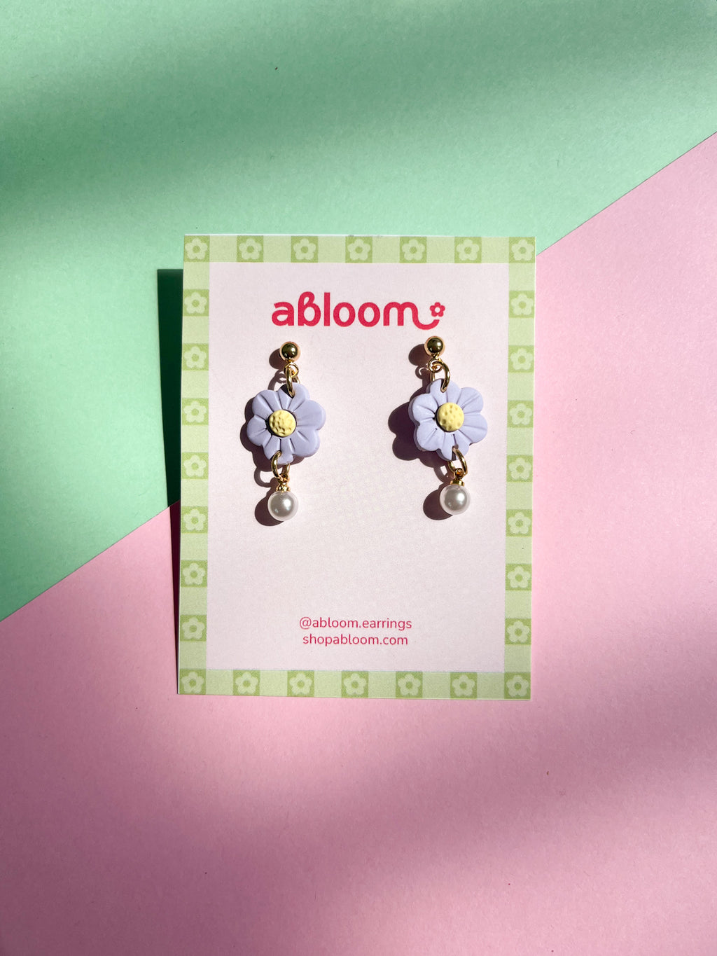 Flower-shaped earrings on a 'abloom' branded card against a green and pink background