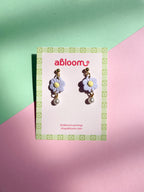 Flower-shaped earrings on a 'abloom' branded card against a green and pink background