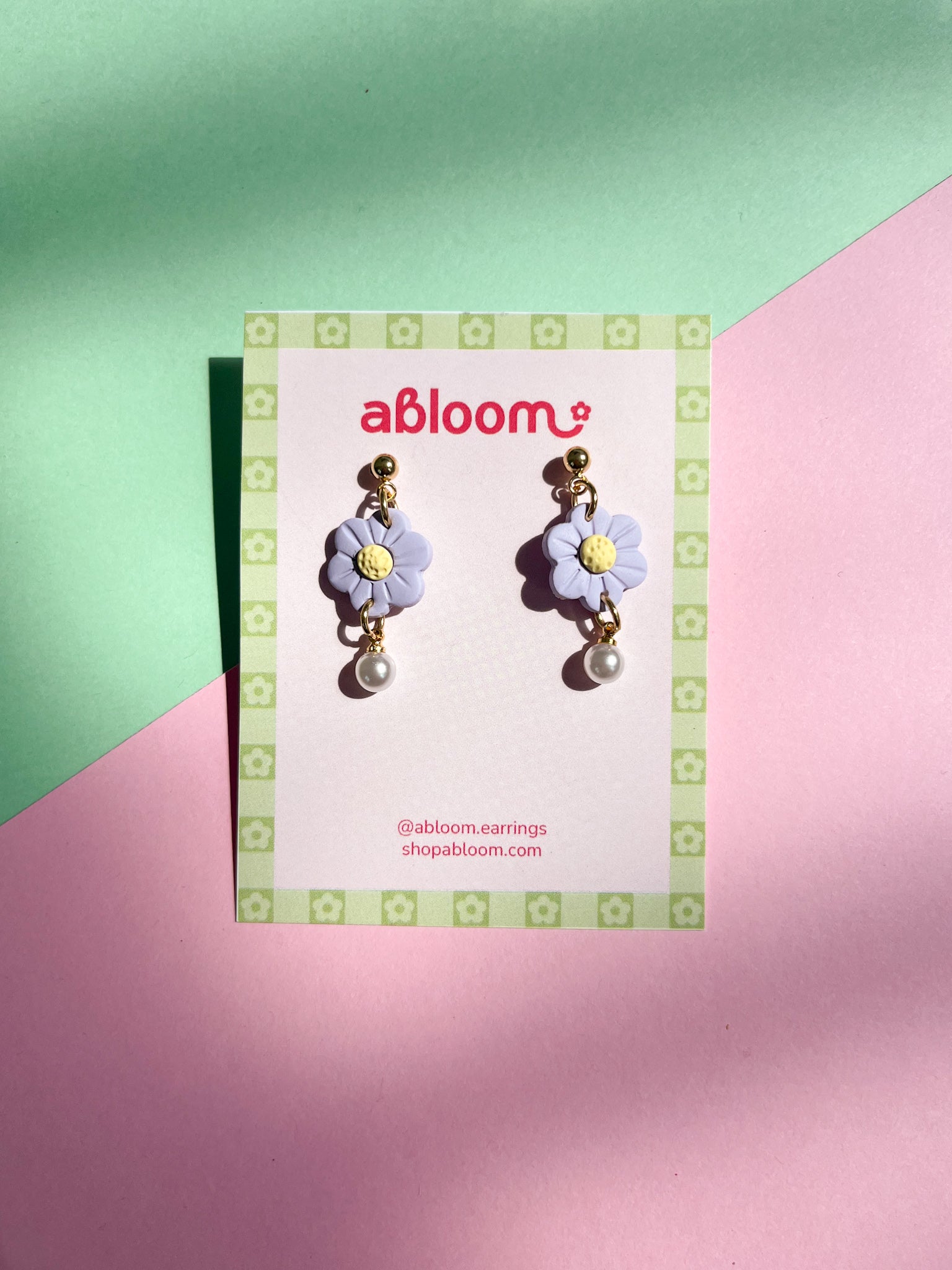 Flower-shaped earrings on a 'abloom' branded card against a green and pink background
