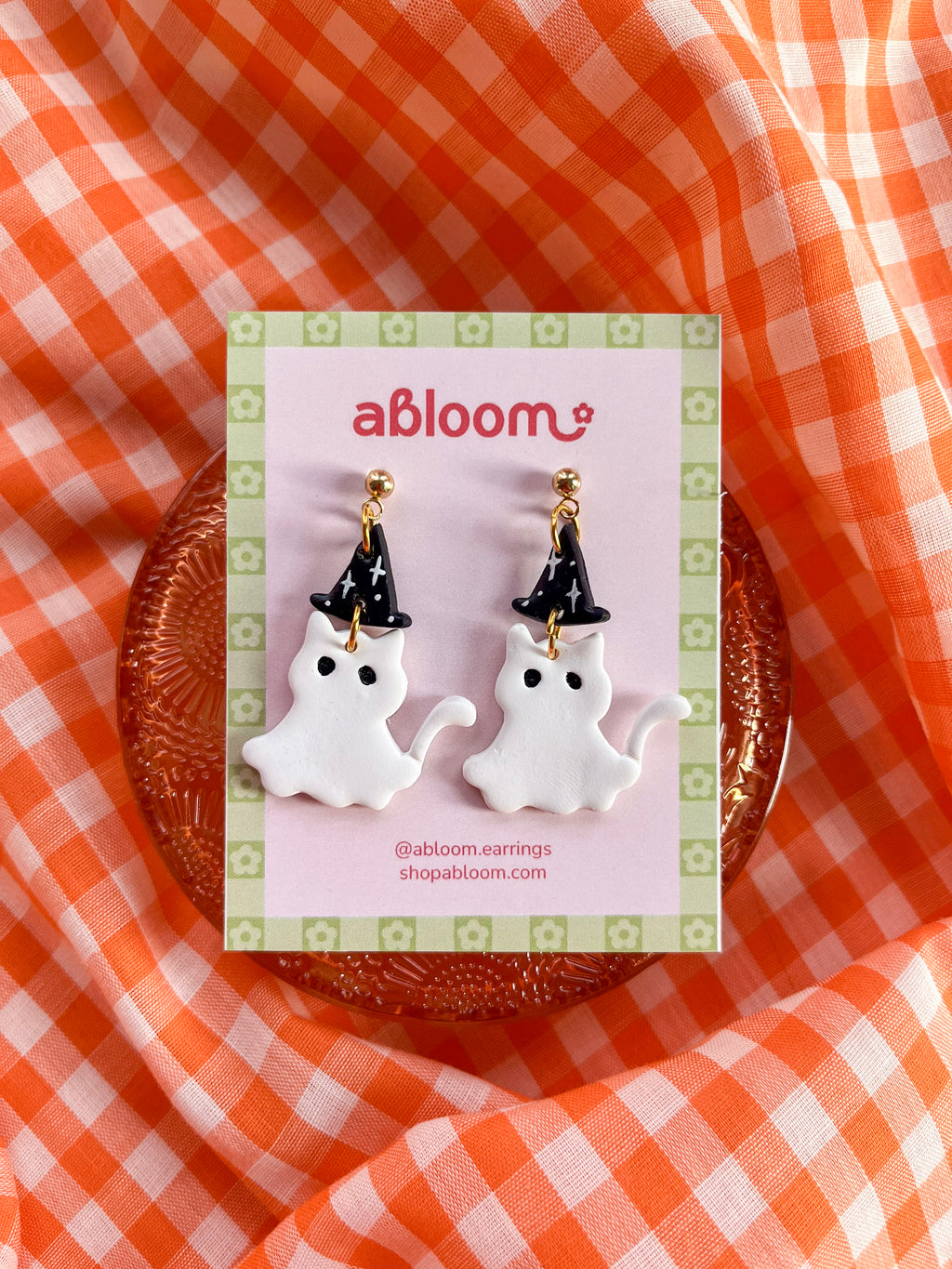 A pair of white cat ghost earrings wearing a witch hat 