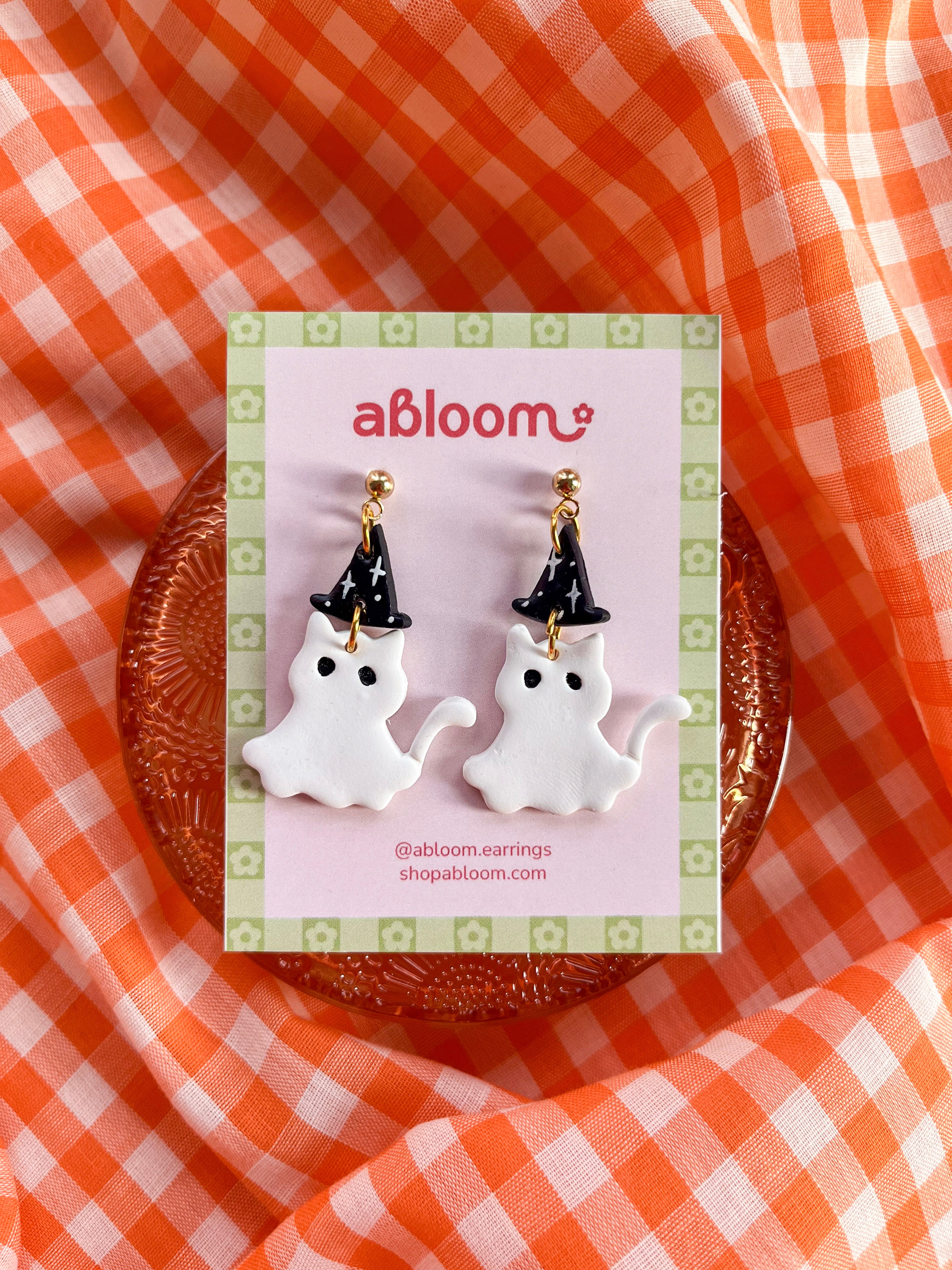 A pair of white cat ghost earrings wearing a witch hat 