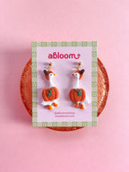 A pair of whimsical polymer clay earrings of white geese in a orange pumpkin costume