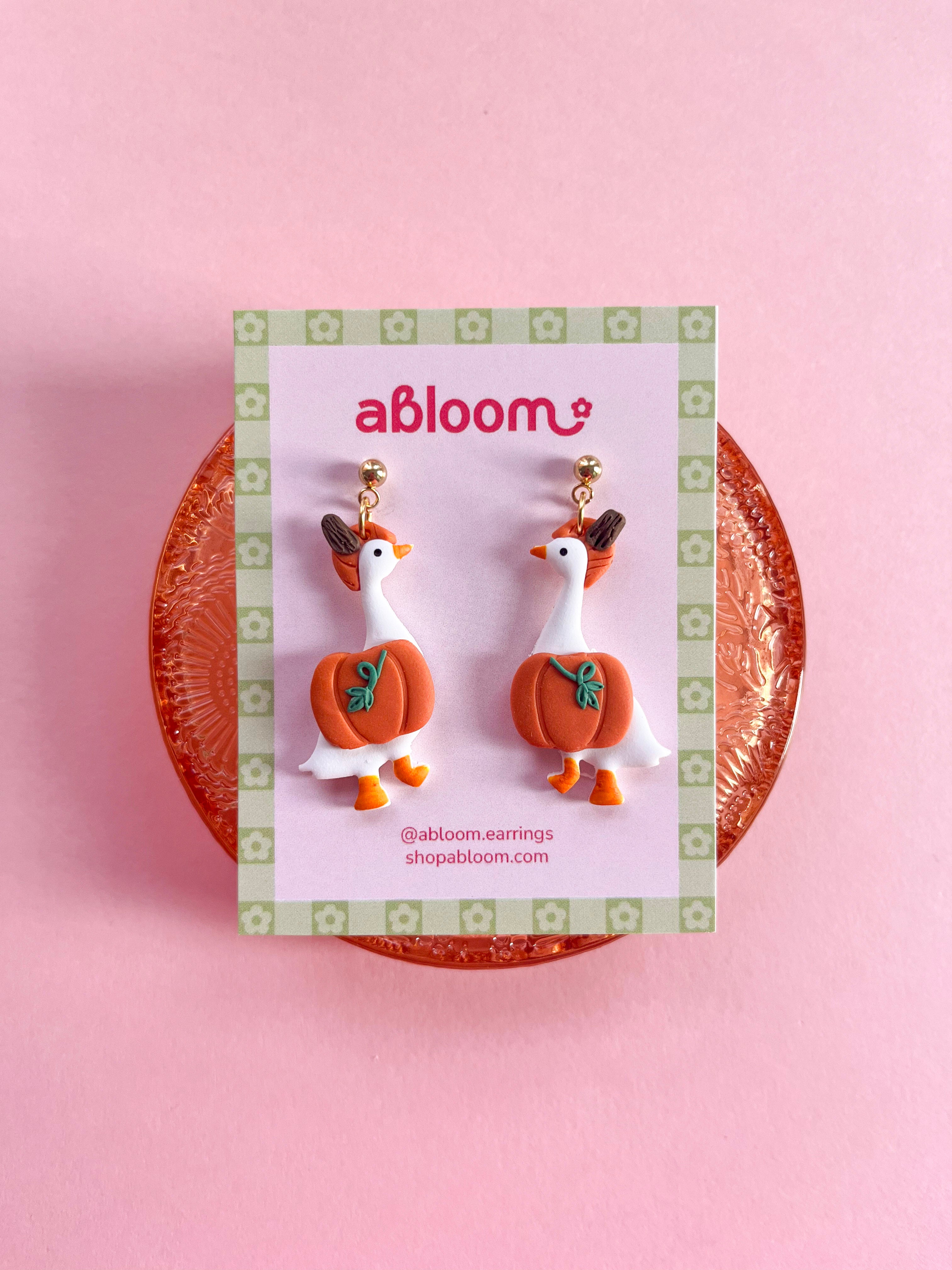 A pair of whimsical polymer clay earrings of white geese in a orange pumpkin costume