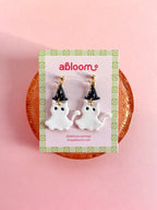 A pair of white cat ghost earrings wearing a witch hat