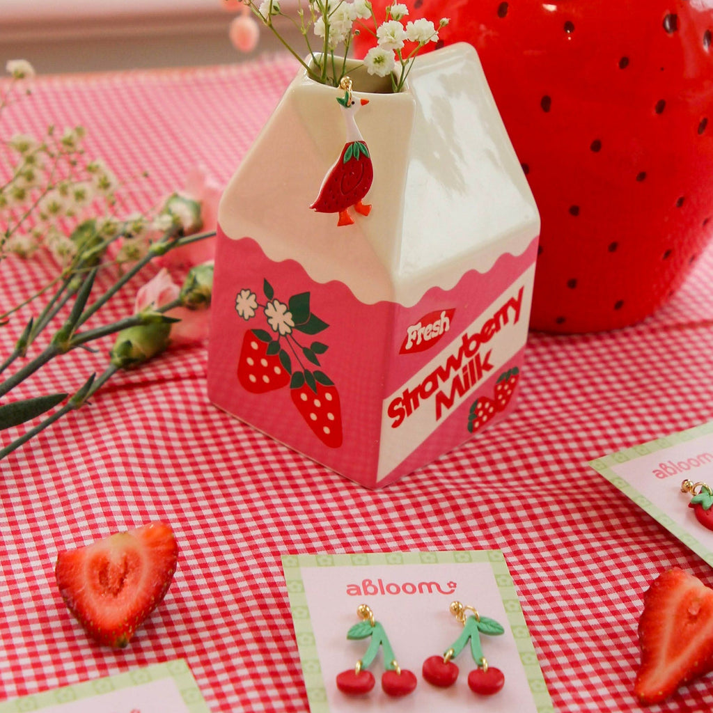 Strawberry-themed milk carton with flowers on a red and white checkered tablecloth.