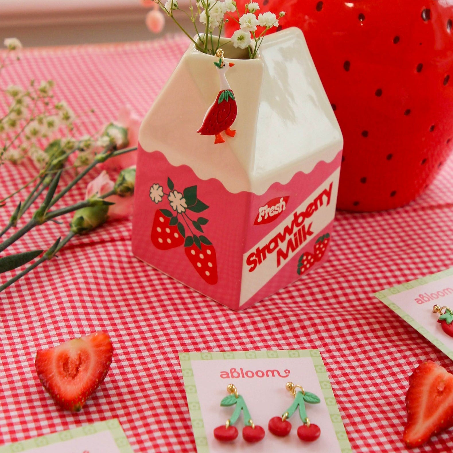 Strawberry-themed milk carton with flowers on a red and white checkered tablecloth.