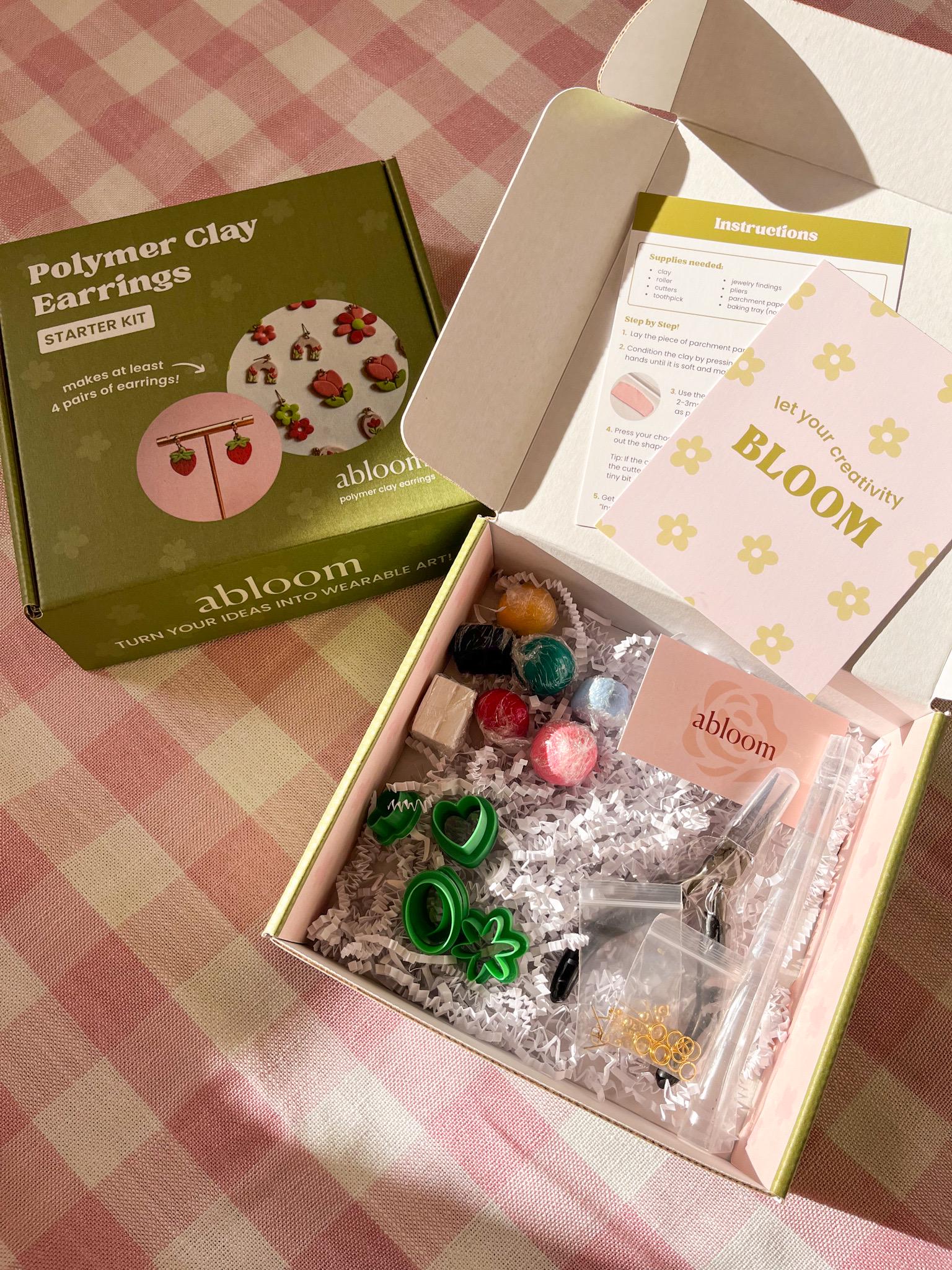 Open box containing polymer clay earrings kit with 'abloom' branding on a checkered tablecloth.