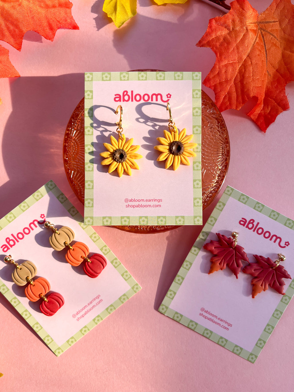 Three pairs of colorful autumn-themed dangle earrings displayed on branded abloom cards