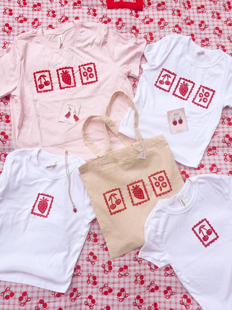 T-shirts and a tote bag with red and white designs on a red and white checkered background