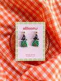 A pair of small frog-shaped earrings wearing a witch hat